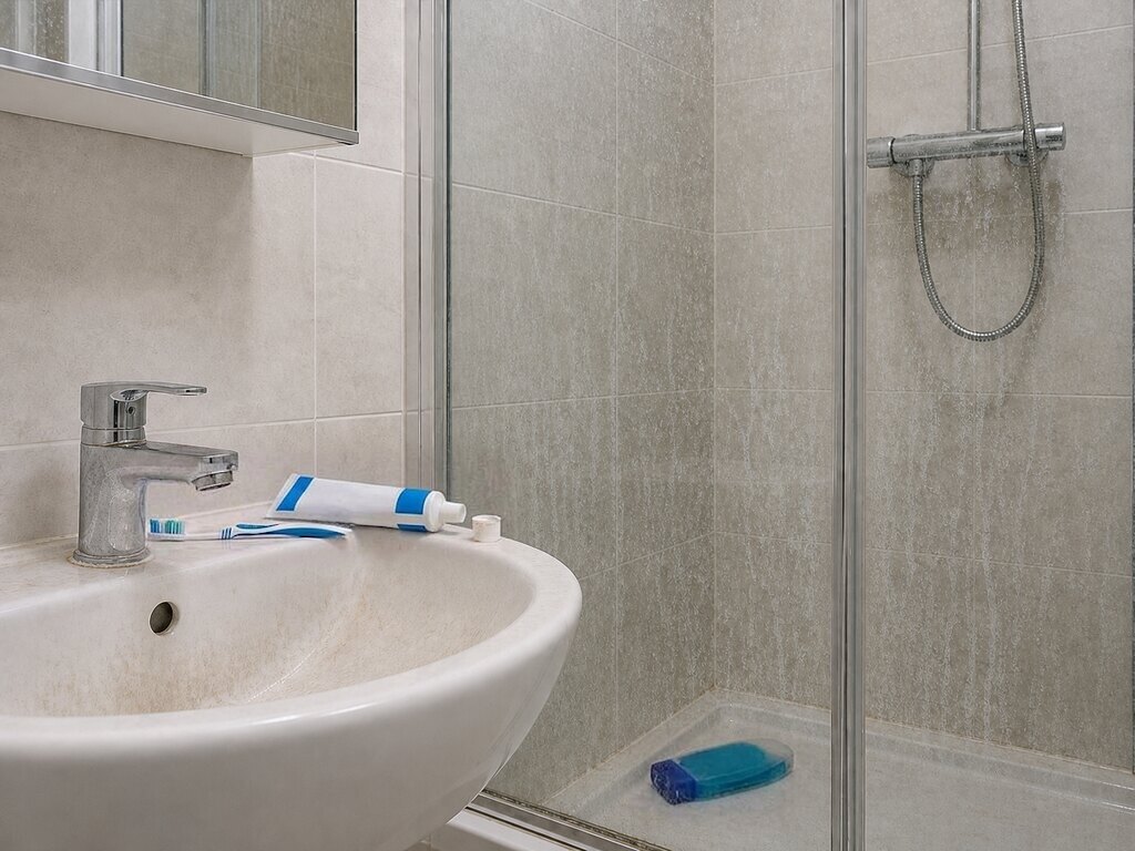 Before: a toothbrush and toothpaste left by the tap, shower gel knocked over in the shower tray, and residue on the tap, basin and shower glass