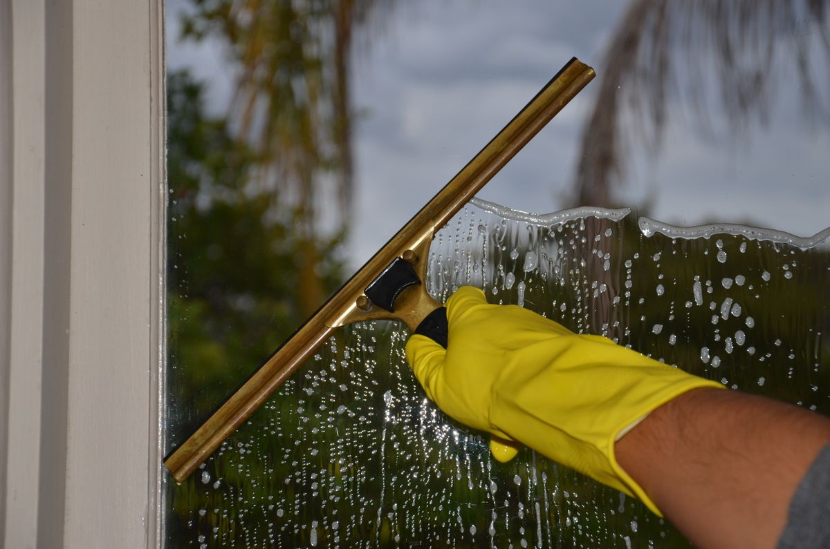 A gloved hand cleaning window glass with a squeegee